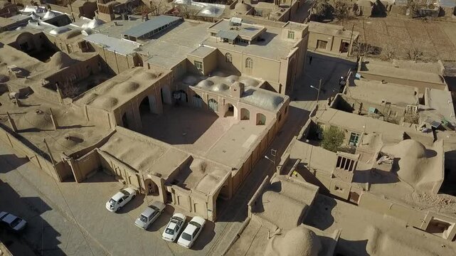 Detailed aerial view of a dense Persian desert village with closely packed adobe rooftops, domes, and windcatchers. The architectural composition reveals ancient Iranian urban design principles