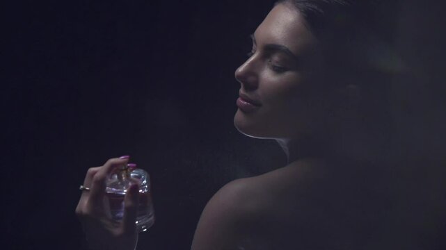 Perfume. Beauty glamour fashion woman applying Perfume. Beautiful model girl holding bottle of perfume on dark background, enjoying aromatic, scented water. Perfumery concept. Spray. Slow motion. 