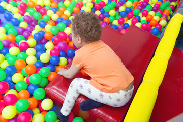 Fototapeta premium A curly-haired baby plays in a multicolored ball pool in a children's playroom