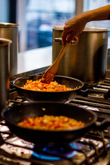 Cooking in a professional kitchen in a cafe. A hand stirs vegetables in a frying pan on a gas stove against the background of pots
