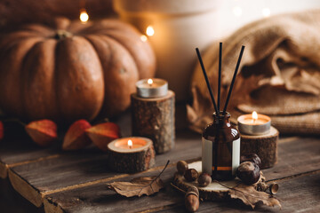 Autumn cozy mood composition with burning candles. Aroma stick reed diffuser, pumpkin on wooden table, knitted warm plaid. Fall hygge home decor, aromatherapy. Relaxed atmosphere in the apartment