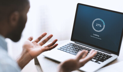 Slow computer software concept. Indignant african american guy looking at laptop with loading...
