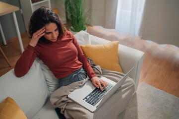 Stressed freelancer working from home having headache using laptop on sofa