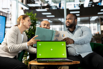 Green screen laptop in front of employees checking progress done on customer commissioned project. Chroma key notebook next to office clerks reading data statistics on paperwork after business audit