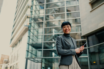 Smiling businesswoman holding tablet in front of office building