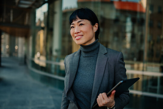 Smiling businesswoman holding tablet and walking in city center