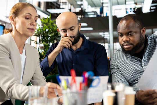 Multiethnic employees in company office checking progress on customer commissioned project. Team of multiracial bookkeepers comparing key data statistics after business audit