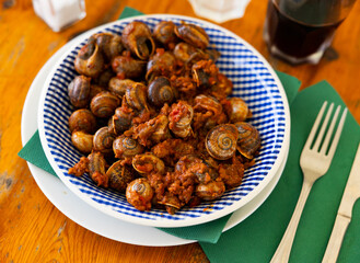 Plate contains dish of Mediterranean cuisine - snails with minced meat and tomato sauce. Gastronourism, national festive Spanish food.