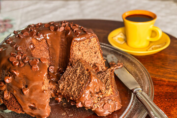 Chocolate cake with syrup and chocolate drops and coffee cup in the background