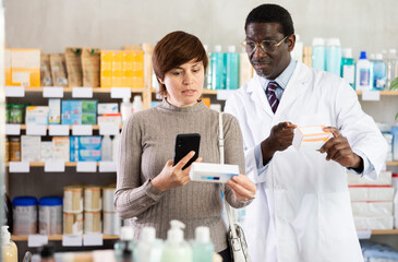 Obraz premium Adult woman buyer scanning qr code for ointment with adult man pharmacist in pharmacy