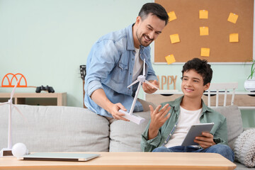 Father with wind turbine model and his son using tablet computer at home