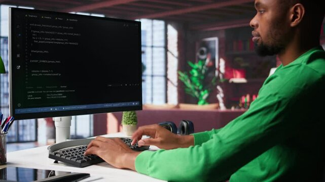 Male programmer types code on computer and running script, programming language. African american IT expert in modern loft fixing errors within the software, implementing new features. Camera A.