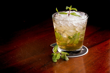 cocktail glass with whiskey and ice gin and mint in pub on black background
