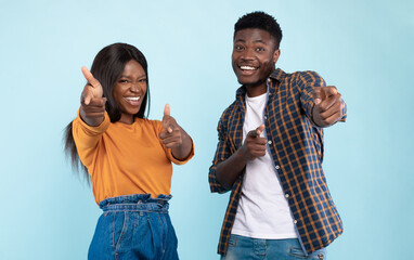 Hey, You. Portrait of cheerful African American guy and lady pointing two index fingers at camera,...