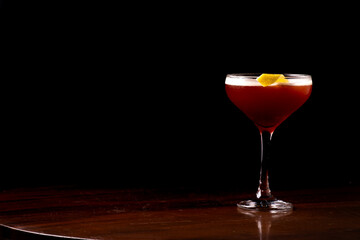 glass of elegant red fruit martini drink with orange sliver garnish
