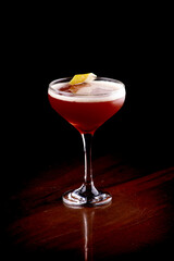 glass of elegant red fruit martini drink with orange sliver garnish close-up