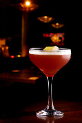 glass of elegant red fruit martini drink with orange sliver garnish in pub with blurred background