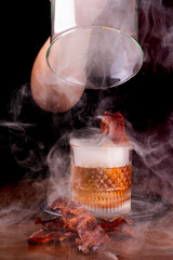 old fashioned cocktail smoked in the smoker with lots of smoke crispy bacon slices