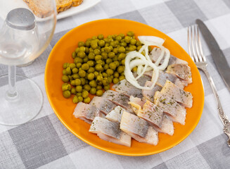Pieces of herring served on plate with pea and onion. Appetizer fish on table.