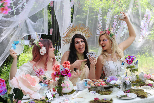 Drei als Elfen oder Feen verkleidete Frauen streiten sich um ein Kartenspiel