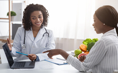 Personal nutrition plan. African american woman dietologist consulting patient, using laptop,...