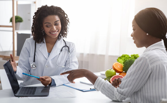 Personal nutrition plan. African american woman dietologist consulting patient, using laptop, clinic interior
