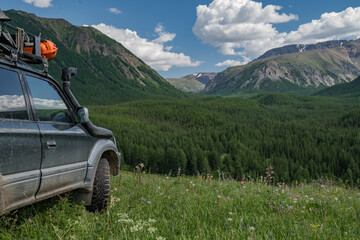 An off-road family car is parked in a green meadow overlooking a forest and a mountain gorge. Mud wheels for an SUV on a background of green vegetation. A family car for traveling.