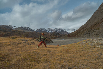 A traveler in trekking clothes walks from left to right holding trekking poles in his hands. The action takes place against the backdrop of mountains, in autumn. Autumn mountains.