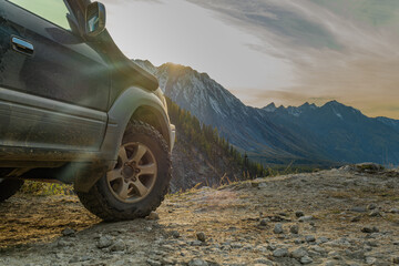 An off-road car stands on a mountainside during the golden hour, showing off off-road tires against the backdrop of a valley with mountains. Mud tires on the background of mountains.