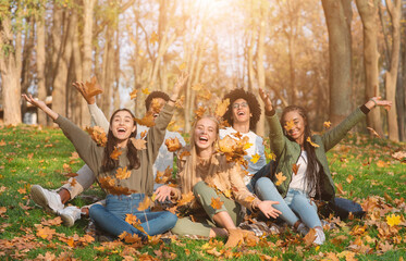 Group of cheerful international friends playing with autumn leaves in public park, taking autumn photos together