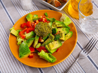 Vegetable side dish, salad of chopped cabbage leafy vegetables, bell pepper, avocado and pesto sauce.