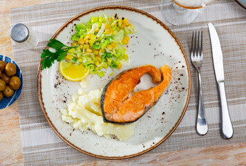 Salmon fillet served with potatoes and fresh vegetable salad on platter