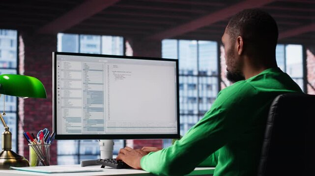 Black IT expert looking at user interface on computer at home office, typing and programming code on terminal window. Coding application used by technician writing script in loft. Camera B.