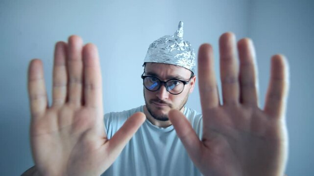 Man wearing a tinfoil hat gestures in disbelief, expressing fear and humor about conspiracy theories