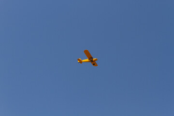 A yellow, single-engine airplane with a high-wing design glides through an expansive blue sky.