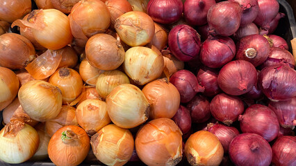 Golden and red onions are stacked high in a bin using close up technique.