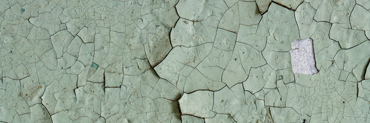 Peeling paint on the wall. Panorama of a concrete wall with old cracked flaking paint. Weathered rough painted surface with patterns of cracks and peeling. Panoramic texture for background and design.