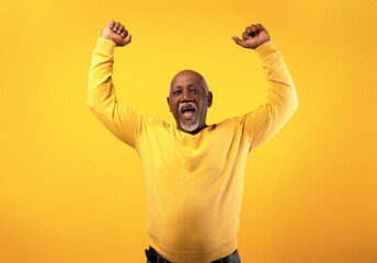 Overjoyed senior black man screaming in excitement, gesturing YES with both hands on orange studio...