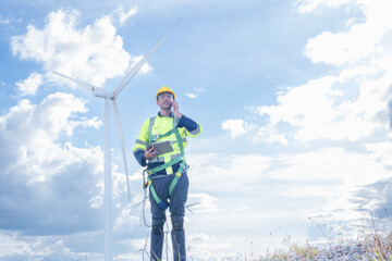 Architectural american engineer in hardhat working with mobile phone on wind turbines at electricity power station background. Renewable energy, wind turbine generate electricity to produce energy .