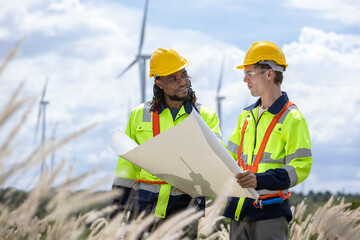Team of African american engineer with blueprint checking wind turbines at windmill field farm....