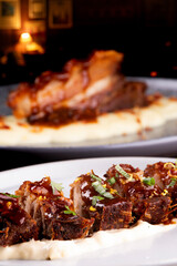 close-up of strips of pork belly on a bed of parmesan cheese and another blurred dish in the background