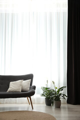 Comfortable sofa near window with elegant curtains in room