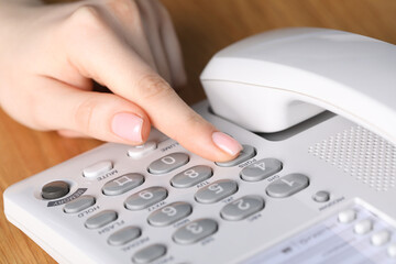 Woman dialing number on telephone at wooden table, closeup