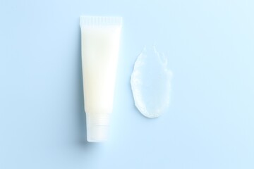 Moisturizing lip balm and tube on light blue background, top view