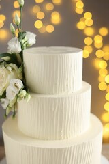 Delicious wedding cake decorated with flowers on grey background with blurred lights, closeup