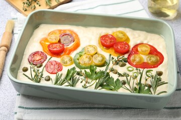 Raw focaccia with vegetables, spices and brush on light grey table, closeup