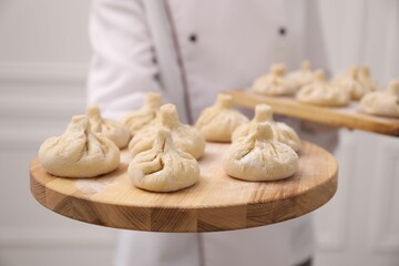 Chef holding board with uncooked khinkali indoors, closeup