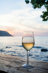 Glass of white wine resting on a wooden table overlooking a tropical sunset seascape