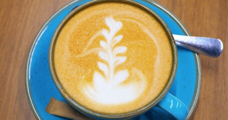 Cups of cappuccino, decorated with latte art and accompanied by small wooden stirrers, sit on vibrant blue saucers, arranged on a warm, wooden table. Concept of coffee consumption