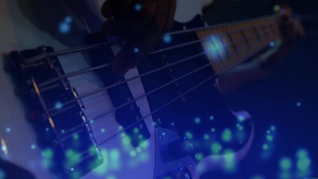 Musician's hand pressing bass guitar strings in music production, floating blue bokeh particles